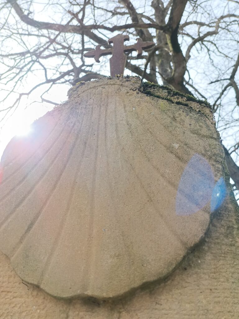 Detailaufnahme eines Pilgersteins mit Muschel und Kreuz im Sonnenlicht