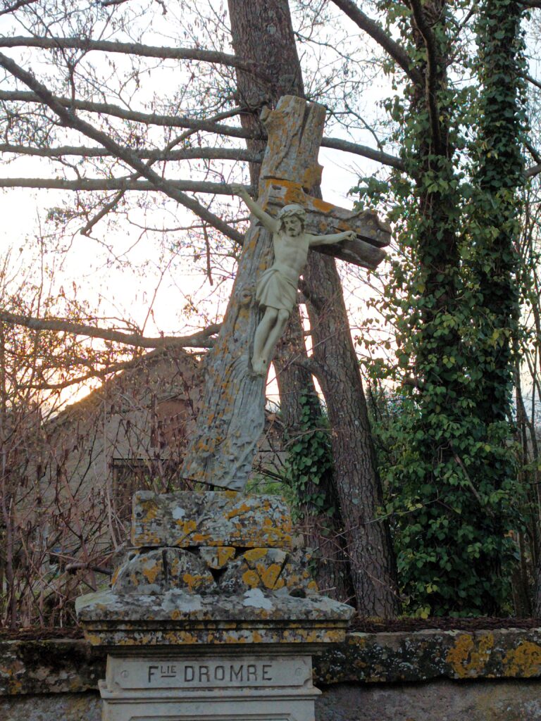 Eine verwitterte Christusstatue auf einem kunstvoll gestalteten Kreuz vor der Église St Rémy.