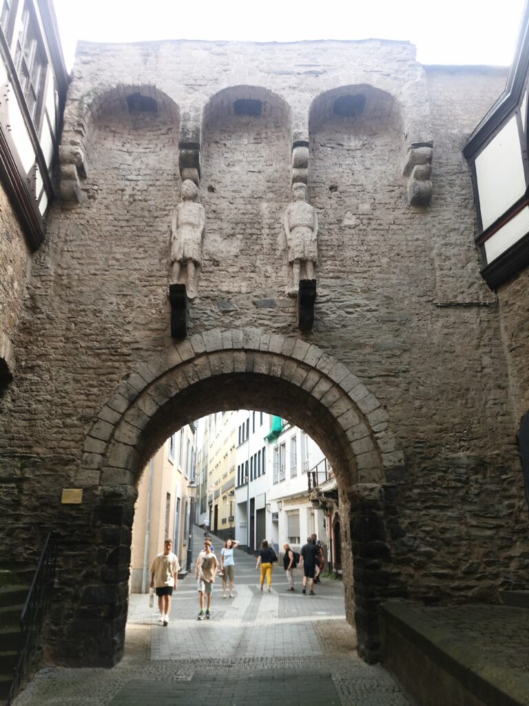 Innenseite des Rheintors in Andernach mit den steinernen Wächterfiguren, Blick durch den Torbogen auf die dahinterliegende Straße.