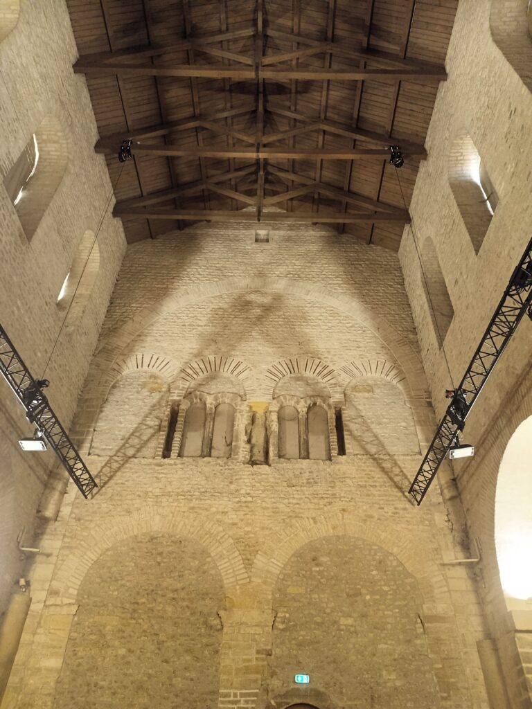 Innenansicht der frühchristlichen Kirche Saint-Pierre-aux-Nonnains mit romanischen Bögen und hölzernem Dachstuhl.