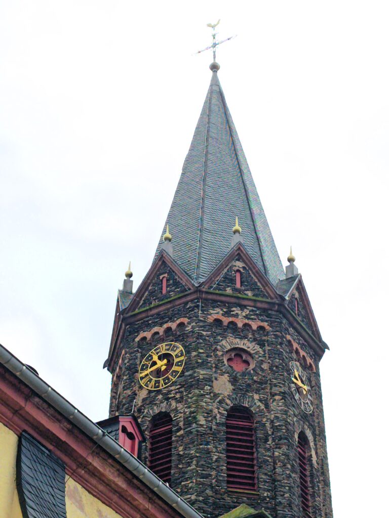 Nahaufnahme des Kirchturms der Kirche St. Petrus in Lieser mit goldener Turmuhr.