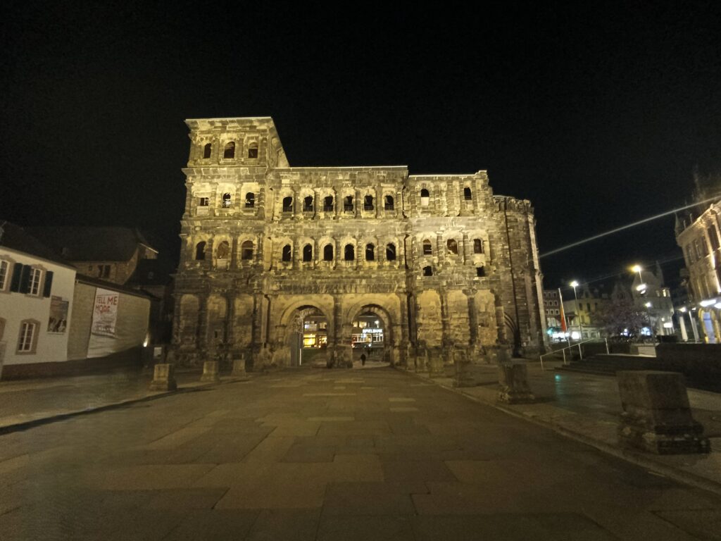 Frontalansicht der Porta Nigra in Trier bei Nacht, beleuchtet durch warmes Licht.