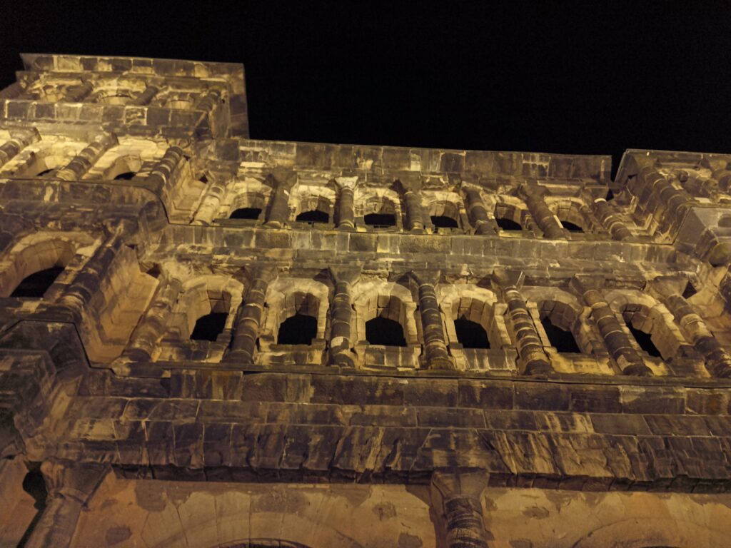 Nahaufnahme der Porta Nigra bei Nacht, mit beleuchteten Bögen und Fensteröffnungen, die die römischen Details betonen.