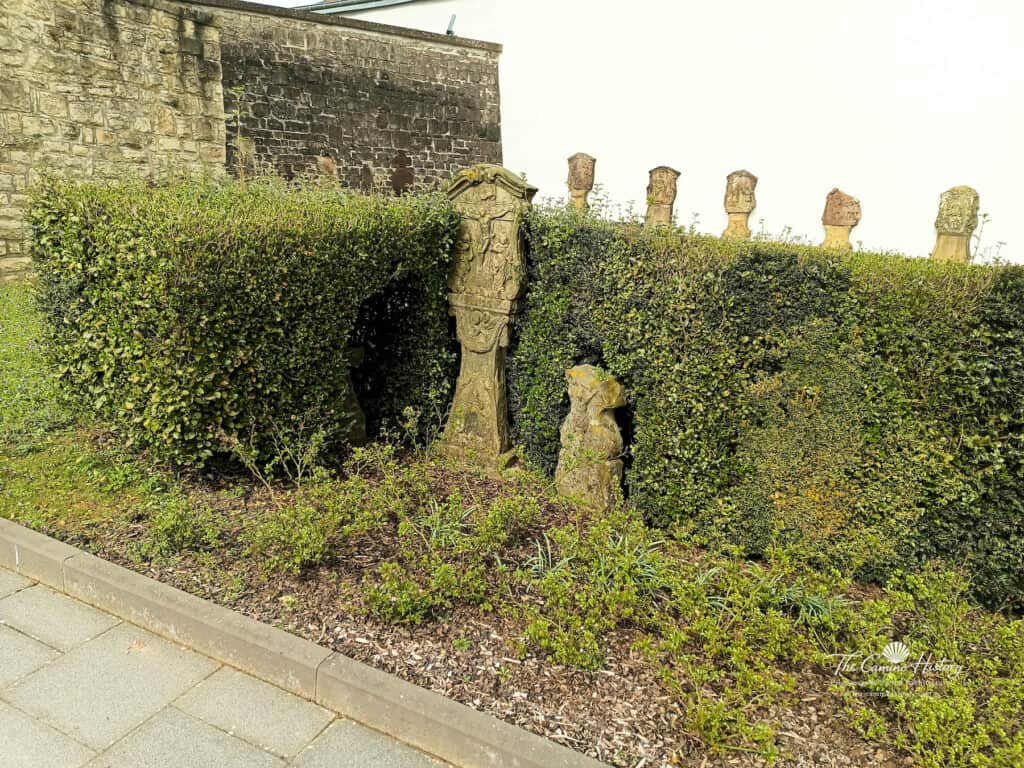 Historische Grabkreuze aus Stein, eingebettet in eine Hecke neben der Pfarrkirche St. Johannes der Täufer in Borg.