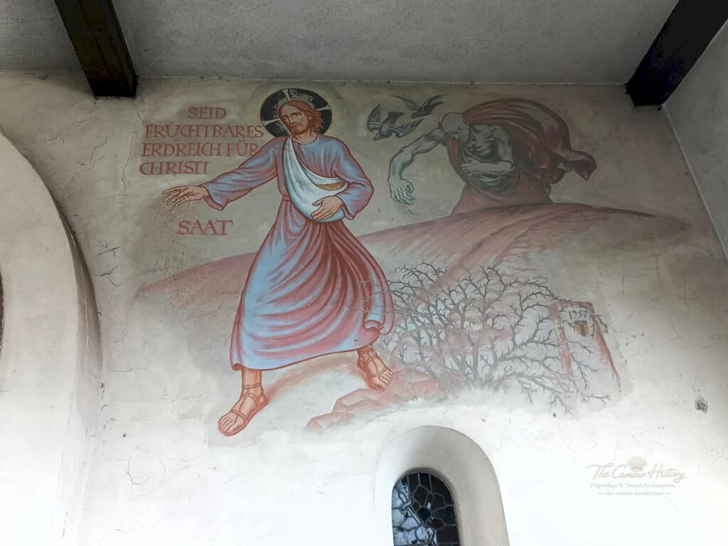 Dieses Wandgemälde in der Pfarrkirche St. Johannes der Täufer in Borg zeigt Jesus als Sämann. Die Szene symbolisiert die Aussaat des Glaubens und die Herausforderungen, auf fruchtbarem Boden zu wachsen. Geschaffen wurde die Malerei im Jahr 1957, begleitet von der Inschrift: „Seid fruchtbares Erdreich für Christi Saat.