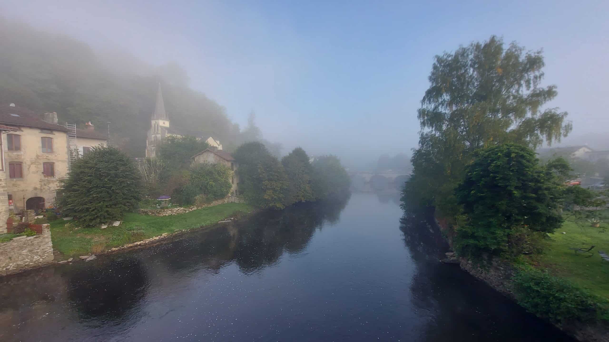 Nebliges Flussufer mit Kirche und alten Häusern