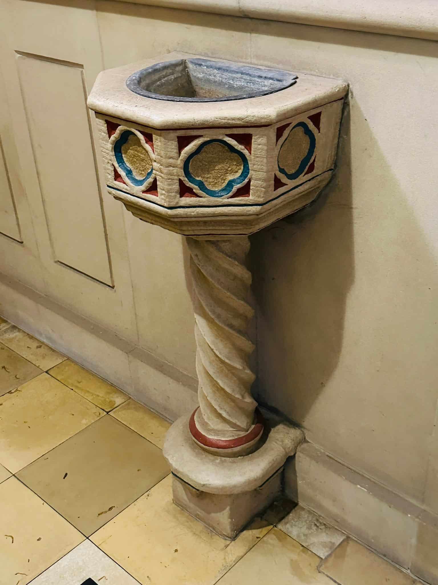 Historisches steinernes Weihwasserbecken mit farbig gefassten Zierfeldern und gedrehtem Schaft