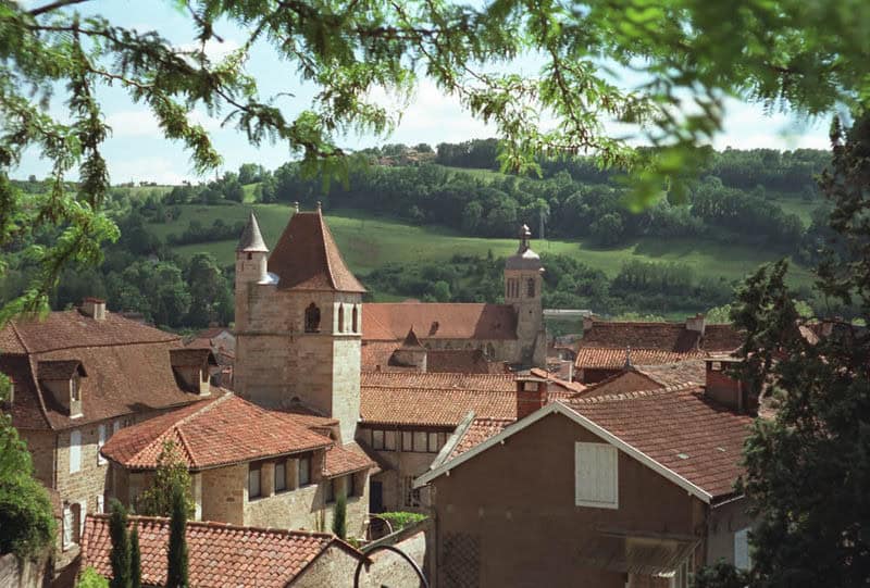Historische Altstadt von Figeac mit roten Ziegeldächern und Kirchtürmen zwischen grünen Hügeln