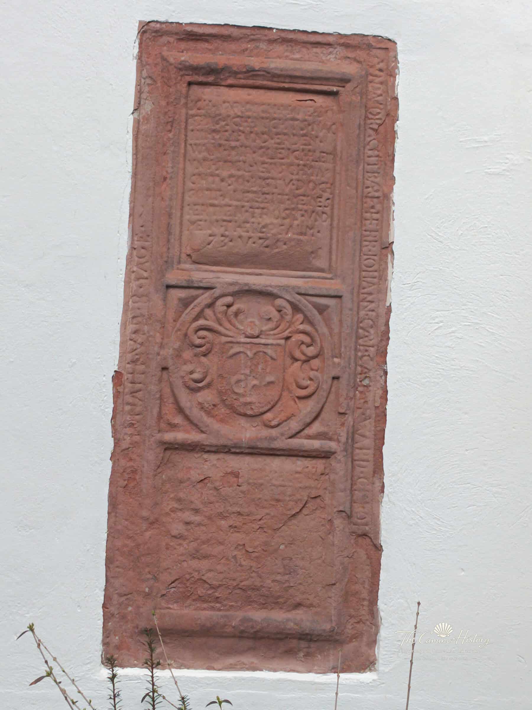 Historische Sandstein-Gedenkplatte mit Inschrift und Wappenschild an einer weiß verputzten Wand der Peterskirche in Traben