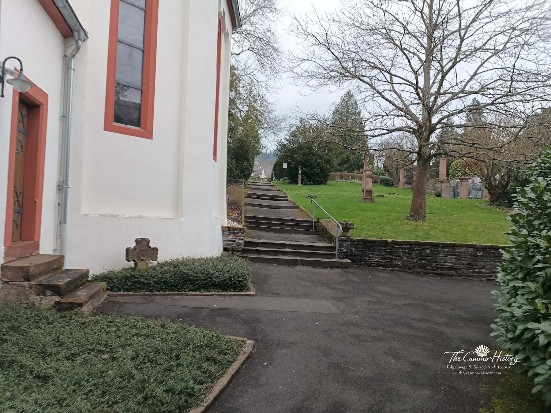 Blick entlang der Außenwand der Peterskirche auf den Kirchhof mit Stufen und historischen Grabdenkmälern