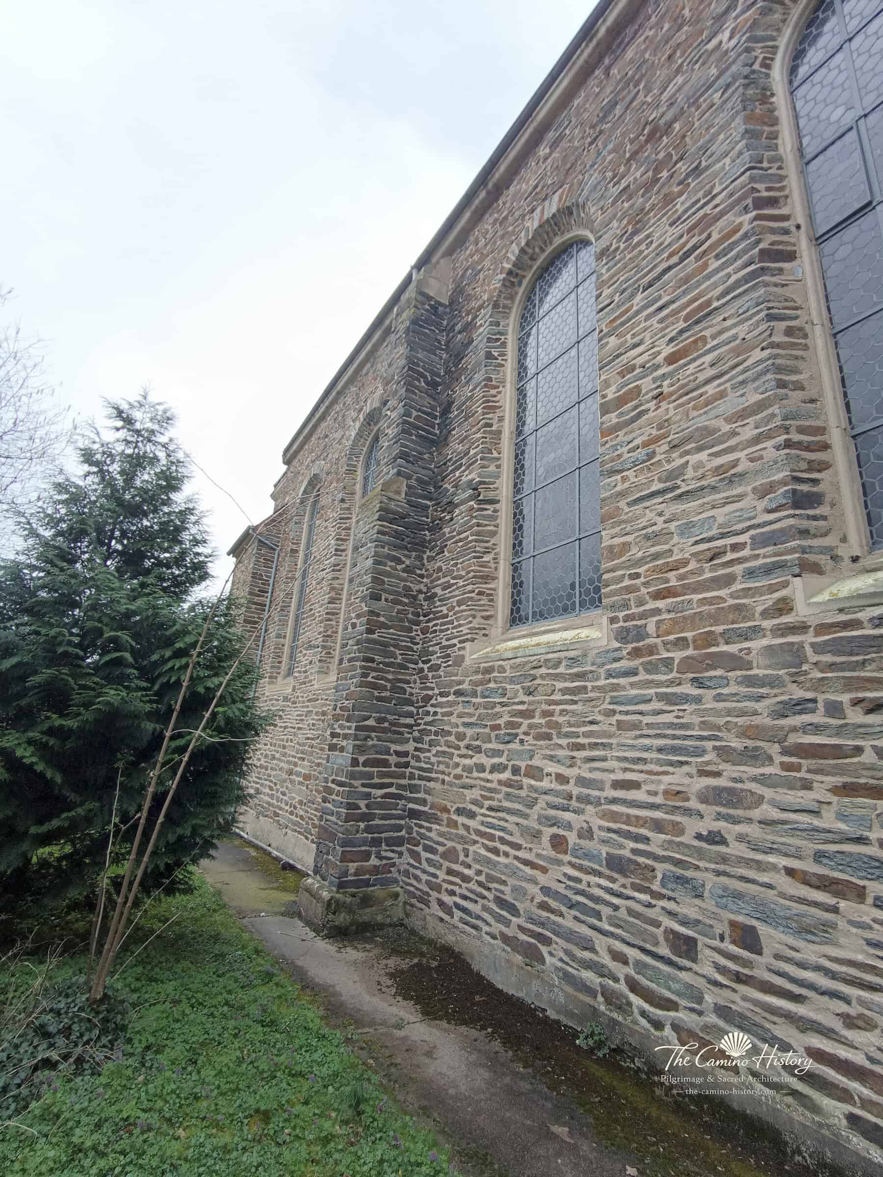 Lange Außenwand von St. Peter und Paul in Traben mit Rundbogenfenstern und Strebepfeilern aus Schiefer.