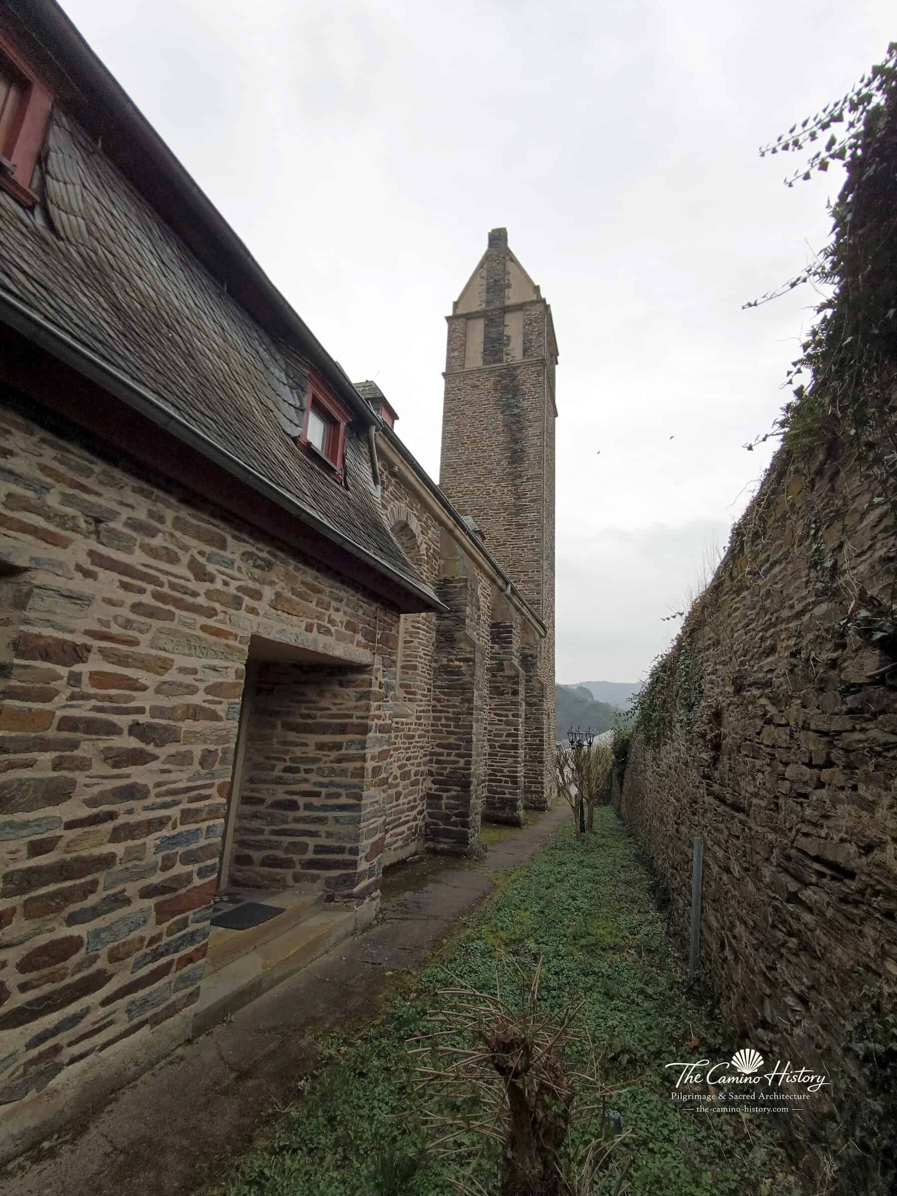 Rückwärtiger Blick auf den rechteckigen Kirchturm von St. Peter und Paul in Traben entlang einer schmalen Gasse.