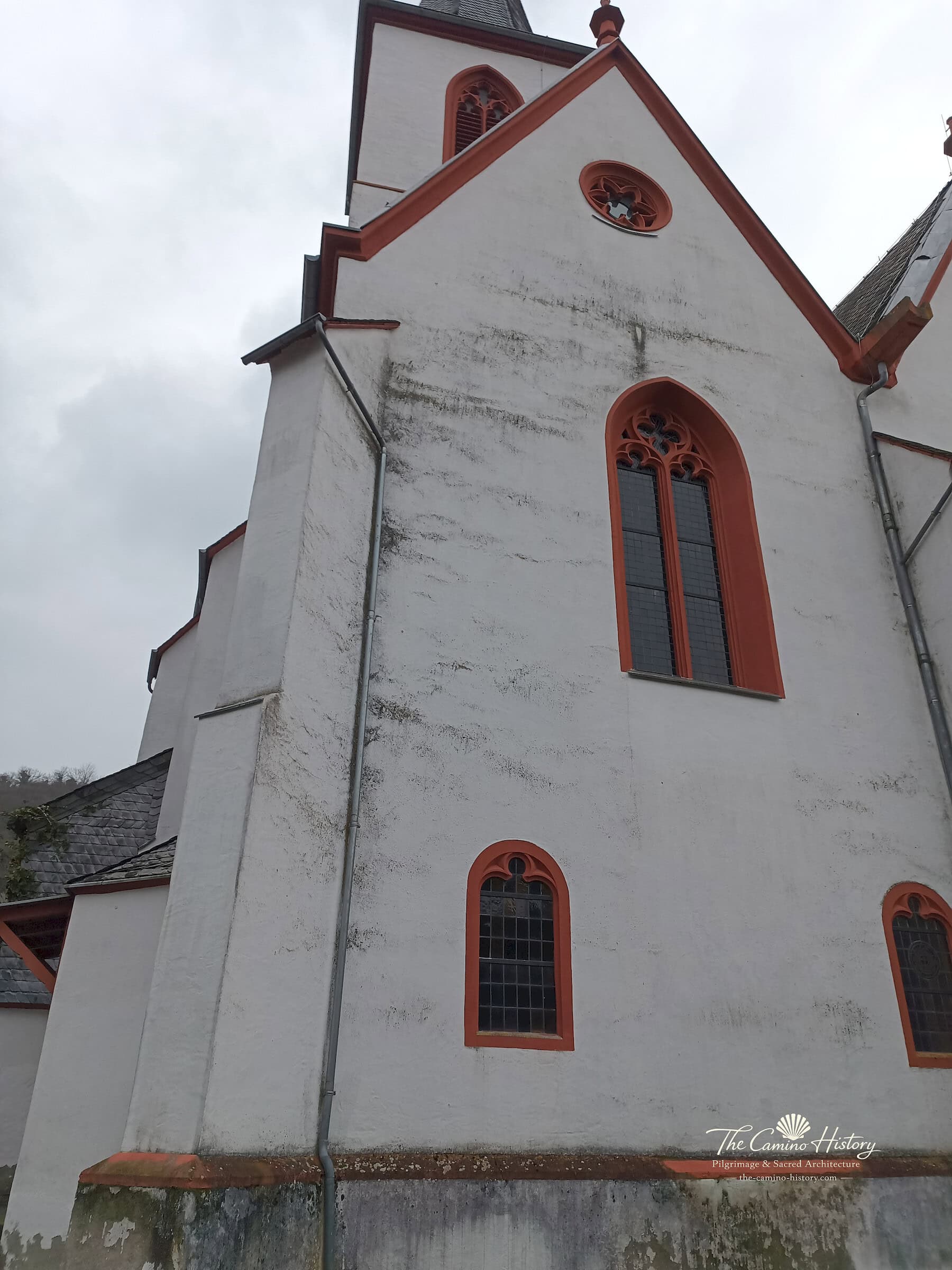 Trarbach – Evangelische Kirche (ehemals St. Nikolaus) 5 Nahansicht eines verputzten Giebels der evangelischen Kirche Trarbach mit roter Maßwerkrosette und hohen Spitzbogenfenstern