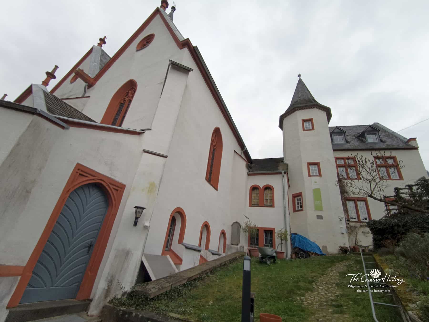 Trarbach – Evangelische Kirche (ehemals St. Nikolaus) 13 Seitliche Giebelwand der evangelischen Kirche in Trarbach mit großer blau-grauer Tür und benachbartem Gebäude mit kleinem Rundturm
