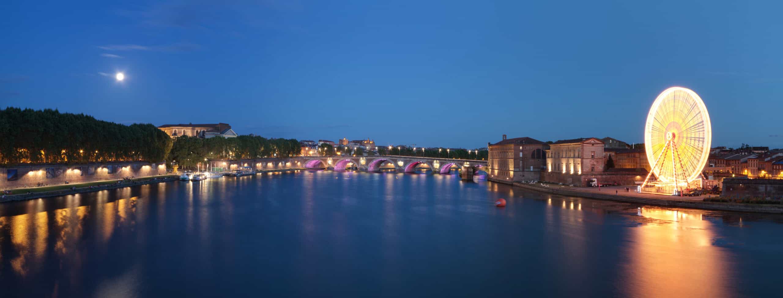 Toulouse in der Abenddämmerung mit Garonne, beleuchteter Brücke und Riesenrad, gesehen vom Pont Saint-Pierre