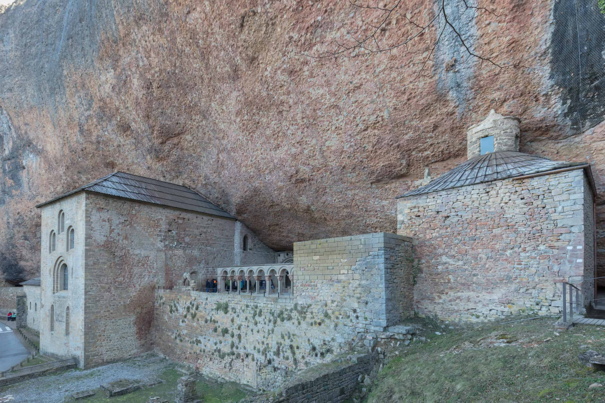 Romanisches Felsenkloster San Juan de la Peña mit steinernen Kirchenbauten und Kreuzgang unter einem gewaltigen Felsüberhang in Aragón, Spanien