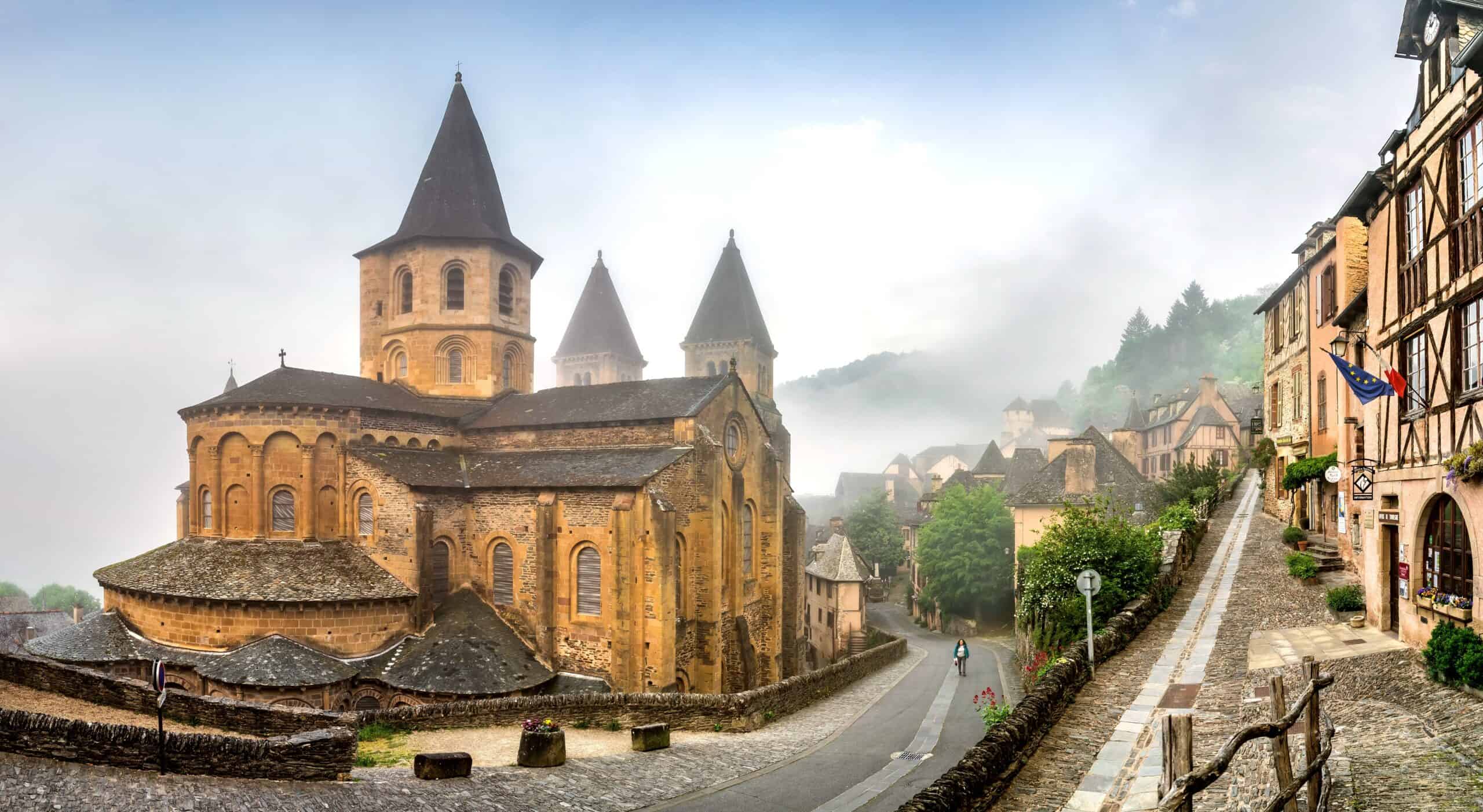 Außenansicht der romanischen Abteikirche Sainte-Foy in Conques mit drei Türmen und steinernen Gassen